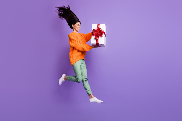 全身尺寸的女孩跳的照片保持包装的礼物盒的生日孤立在充满活力的紫色背景图片下载