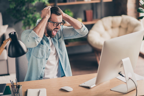 照片肖像的不快乐的男人尖叫在桌面屏幕与双手在桌子在现代工业办公室室内图片下载