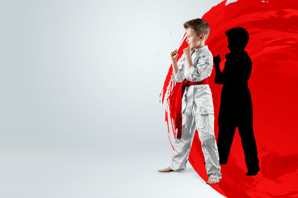 一个男孩穿着白色的和服，带着红色的腰带，背景是一个红色的圆圈，太阳。空手道概念，目标，训练，成就。图片下载