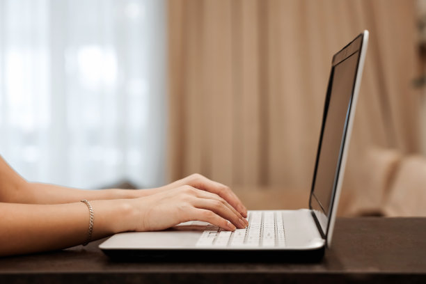 在一个模糊的房间背景下，一个商人的双手在笔记本电脑的键盘上打字。工作场所，办公室，共同工作，商业，金融的概念。图片下载