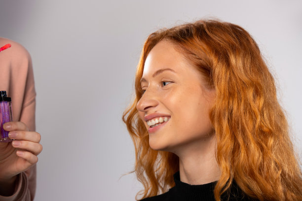 一个微笑的红头发女孩的肖像，看着一边在白色的背景。化妆和美容概念。图片下载