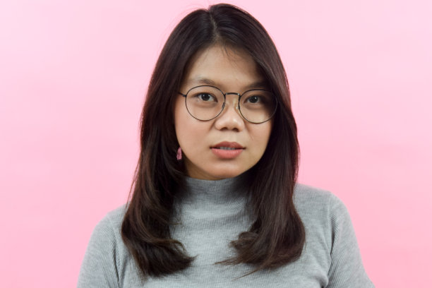 看着镜头严肃的脸，美丽的亚洲(印尼)妇女穿着灰色的高领衬衫孤立在粉红色的背景图片下载