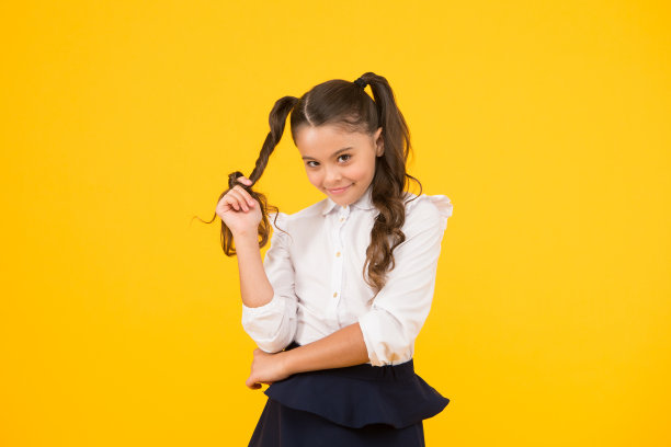 适度的发型。黄色的背景上，可爱的小学生卷发绕着手指。梳着马尾辫的时尚女孩。小孩子为学校设计发型图片下载