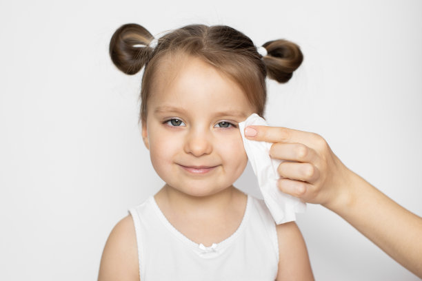 卫生，日常生活，皮肤护理。妈妈的手用湿纸巾擦拭宝宝的皮肤。小女孩对着镜头微笑，享受着洗脸的乐趣。特写肖像在白色的背景图片下载