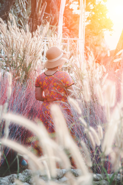 一位亚洲妇女穿着红色的衣服，戴着一顶帽子，愉快地站在花园里休息。图片下载