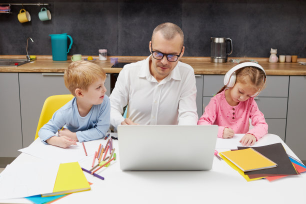 父亲在封锁隔离和学校关闭期间在家工作。冠状病毒的爆发。年轻的自由商人在笔记本电脑上工作，孩子们在周围玩耍。图片下载