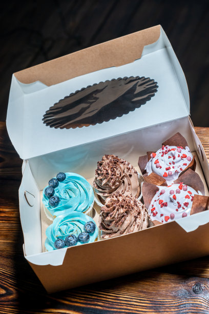 近距离观看自制的各种颜色的纸杯蛋糕，有蓝色的奶油奶酪，可可和白色的纸盒，放在深棕色的木桌上图片下载