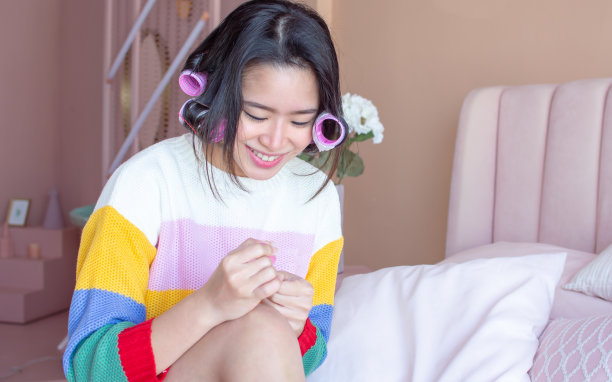 亚洲女人的肖像卷她的头发和刷她的指甲在粉红色的卧室图片下载