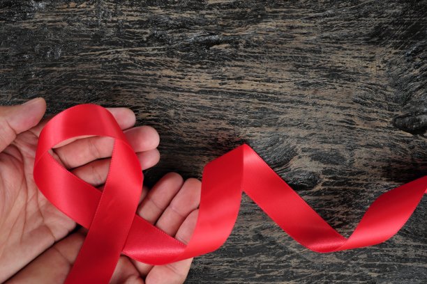 俯视图的男性手拿着红色的丝带在深色的木材背景。认识艾滋病、艾滋病毒、心脏病和中风的概念。图片下载