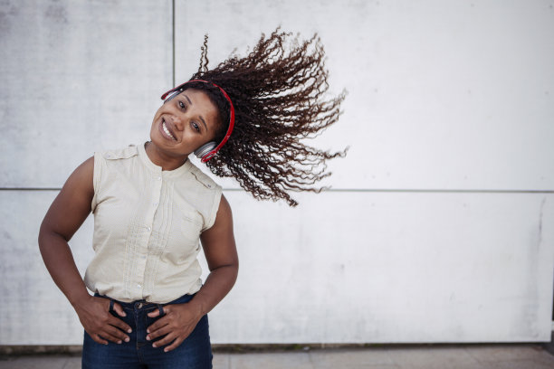 一名黑人妇女在用无线耳机听音乐，摇晃着她的头发。副本的空间。图片下载