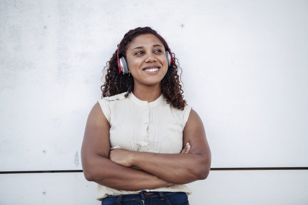 一名黑人妇女正用无线耳机听着音乐，面带微笑。副本的空间。图片下载