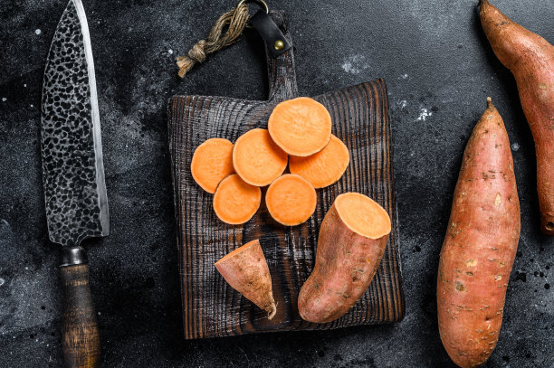 木砧板上的红薯。黑色背景。俯视图图片下载