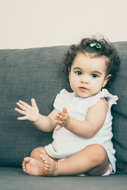 可爱的卷发婴儿，穿着淡蓝色的衣服，坐在灰色的沙发上图片下载
