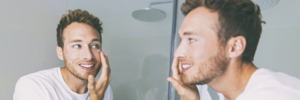 男人在浴室的镜子横幅上涂奶油。小伙子在眼部涂抹抗衰老的保湿产品进行面部护理。男性美容晨间例行在家生活方式图片下载