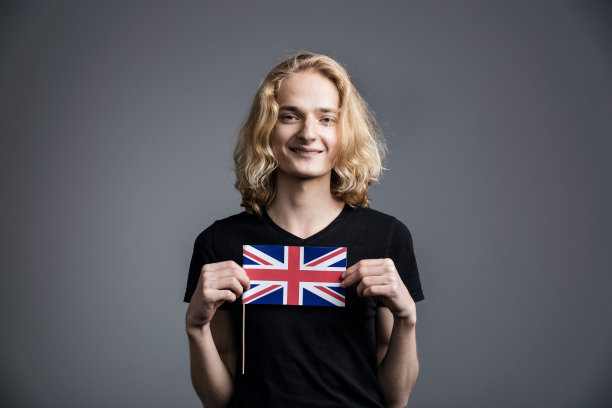 一名身穿核t恤、一头金发的年轻人微笑着在灰色背景上挥舞着英国国旗图片下载