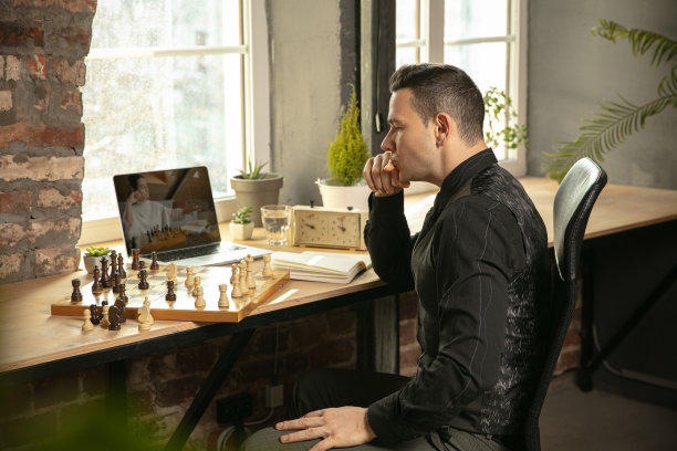 年轻的白种人棋手下棋在线使用笔记本电脑。图片下载