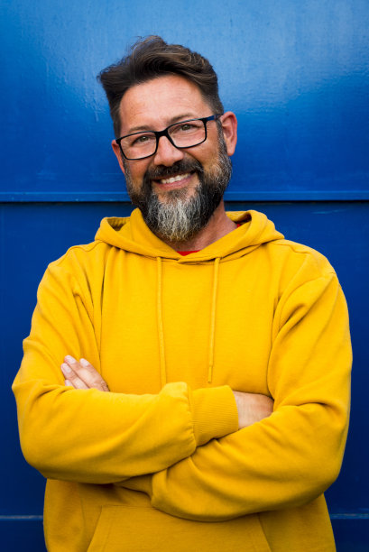 快乐和开朗英俊的成年男子的肖像微笑-彩色的黄色毛衣和蓝色的墙壁背景-年轻的白人男性戴着眼镜享受相机图片下载