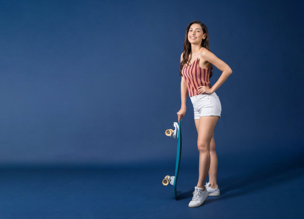 快乐的年轻亚洲女人站着和持有冲浪板或滑板在蓝色的背景图片下载