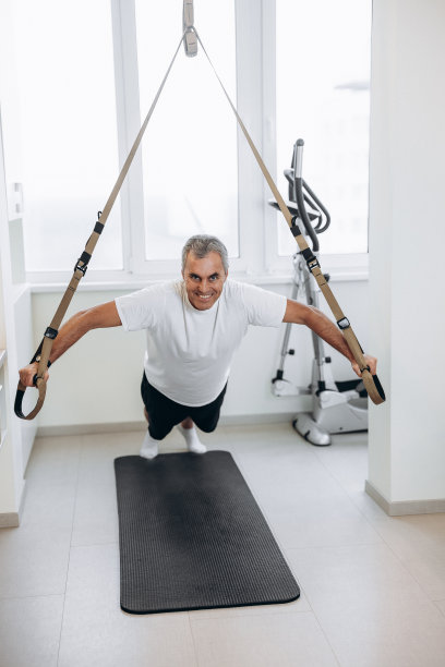 快乐的老运动员锻炼身体。完整的长度。强壮的人在做俯卧撑时用健身带进行悬挂训练。在家锻炼。积极健康的生活方式。图片下载