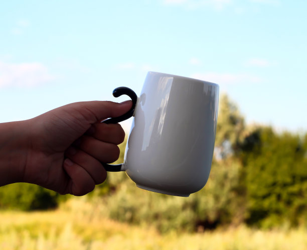 白色的杯子在一个人的手中，以自然为背景。图片下载