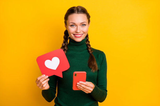 照片肖像快乐的女人与辫子显示心脏图标保持手机孤立鲜明的黄色背景图片下载