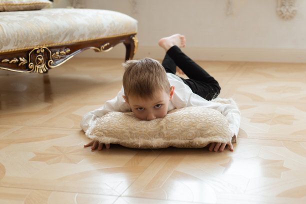 一个小男孩在地板上放纵地躺着。躺在枕头上。图片下载