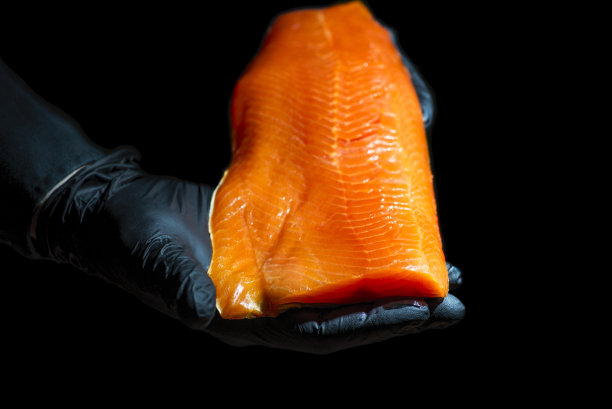 厨师穿着黑色衬衫，戴着黑色乳胶手套，手里拿着一大块鲑鱼片。烹饪过程。图片下载