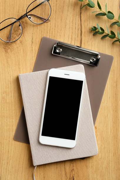 木制的办公桌，有智能手机，纸笔记本，剪贴板，女性眼镜，桉树叶。俯视图，平放，复制空间。图片下载