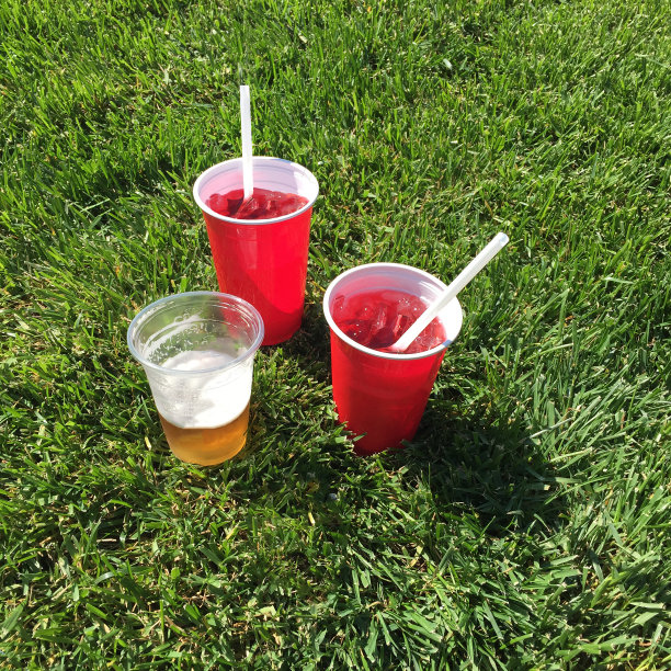 草地上放着一个红色透明的杯子，里面装满了啤酒和各种红色液体图片下载