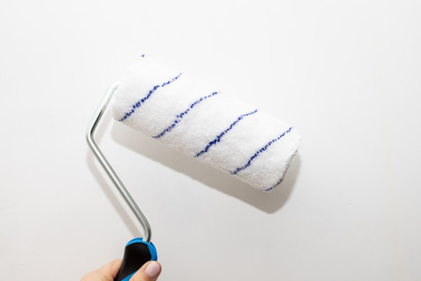 男手拿着一个滚轴，用来刷墙。油漆工把装饰性的油漆涂在墙上。屋内修理。辊壁画。工人准备油漆，家庭翻新。家里装修图片下载