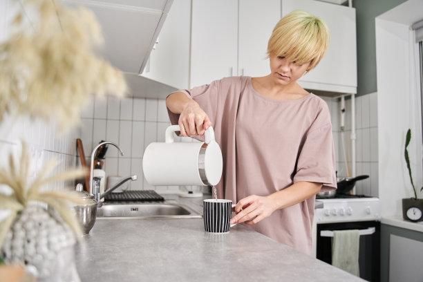 女手持水壶，将水倒入杯中图片下载