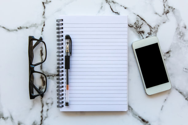 俯视图的空白笔记本，智能手机和眼镜在白色的桌子上。商业计划的概念。图片下载