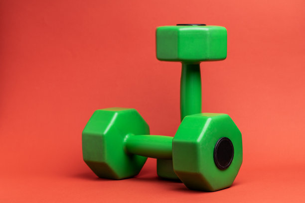 红色背景的绿色塑料运动哑铃，用于力量训练。副本的空间。健康生活方式的运动器材图片下载