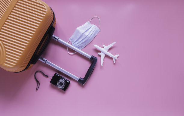 将橙色行李箱和旅行配件平铺在粉红色的背景上，在新冠肺炎流行期间旅行。图片下载