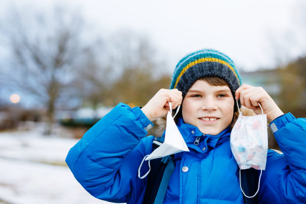 一个戴着医用口罩的小男孩在去学校的路上。孩子背包背包。学生在寒冷的秋冬天穿上暖和的衣服。冠状病毒大流行期间的封锁和隔离时间图片下载
