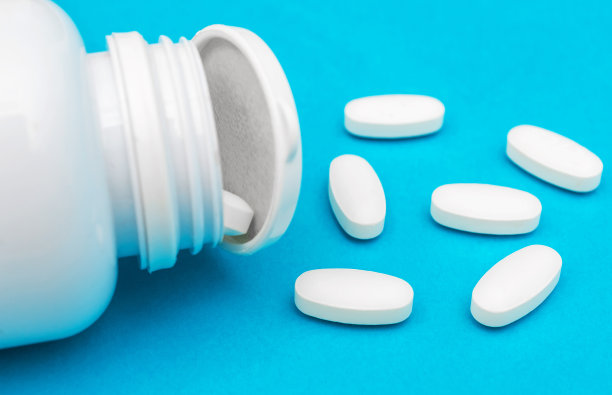 蓝色上散落着白色药丸的塑料医疗容器。图片下载