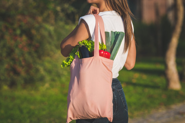年轻女子手提粉色可重复使用的纺织品购物袋，里面装着新鲜的有机蔬菜。以植物为基础的纯素饮食。健康排毒清洁饮食。零浪费，无塑料概念图片下载