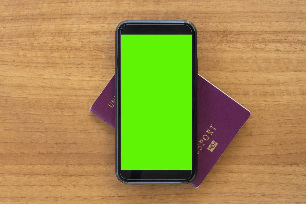 一张木桌上放着一本护照和一部绿色屏幕的智能手机。旅行概念与复制空间。图片下载