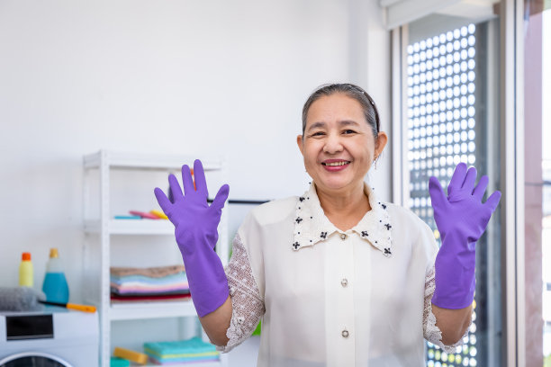 亚洲资深大龄妇女戴着橡胶手套，在洗衣房高傲地举起双手，看着相机，抱着春季大扫除的概念图片下载