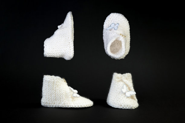 手工编织的白色小童鞋。可爱的新生儿鞋孤立在黑色背景。图片下载