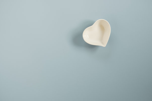 白色小陶瓷心形碗在蓝色和复制空间在蓝色的背景为情人节的概念。图片下载