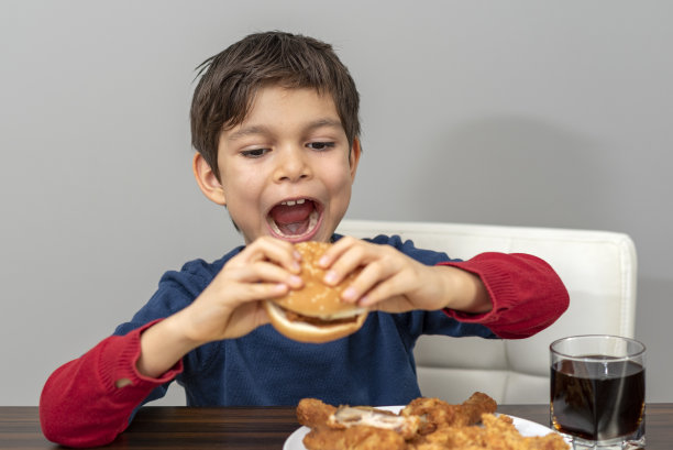小男孩正在吃汉堡包和炸鸡和可乐图片下载