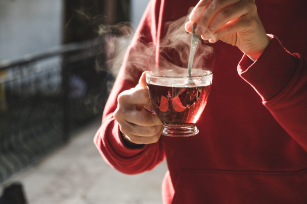 在寒冷的天气里拌热茶的女人。一杯茶正在冒热气。图片下载