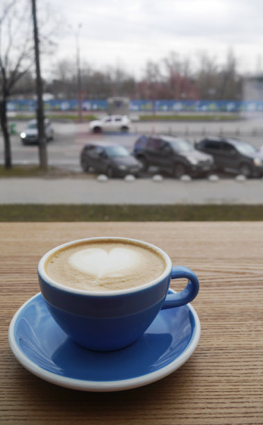 微距照片杯咖啡卡布奇诺或晚与hert泡沫上的木结构桌子上的咖啡。窗外城市喧嚣图片下载