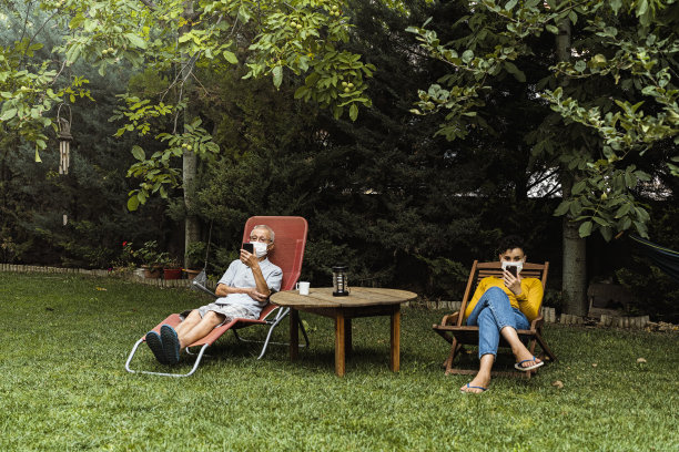 老年男女戴上防护面具，坐在躺椅上，使用手机图片下载