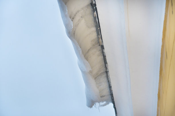 冰雪覆盖屋顶建筑，危险的冰坝悬挂在屋顶上。危险与安全概念图片下载