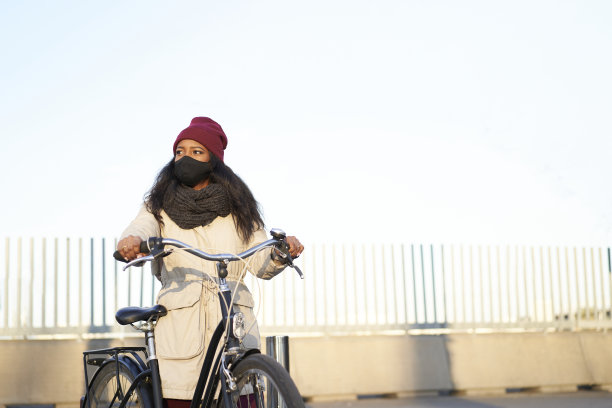 年轻的非洲裔美国妇女骑着自行车，穿着冬天的衣服。干净的背景与复制空间。图片下载