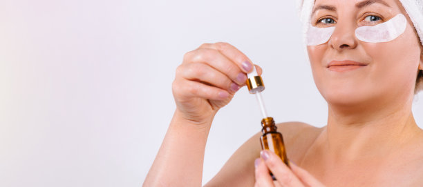 横幅,长格式。一名年长妇女手持提升血清与移液管在她面前的剪裁照片。白色背景和空白侧广告空间。图片下载