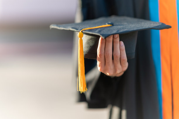 毕业生手拿黑帽子、黄流苏站在大学里图片下载