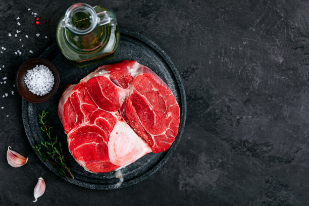 生牛膝肉与调味料在深色的石头背景。图片下载